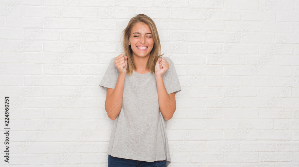 Beautiful young woman over white brick wall excited for success with arms raised celebrating victory smiling. Winner concept. Beautiful young woman over white brick wall excited for success with arms raised celebrating victory smiling. Winner concept.
