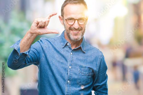Middle age hoary senior man wearing glasses over isolated background smiling and confident gesturing with hand doing size sign with fingers while looking and the camera. Measure concept.