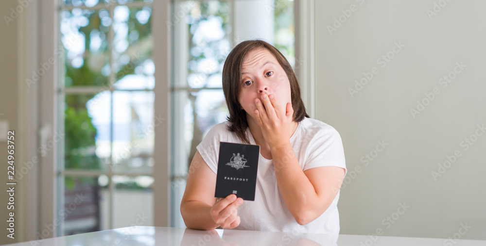 Down syndrome woman at home holding australian passport cover mouth with hand shocked with shame for mistake, expression of fear, scared in silence, secret concept Down syndrome woman at home holding australian passport cover mouth with hand shocked with shame for mistake, expression of fear, scared in silence, secret concept