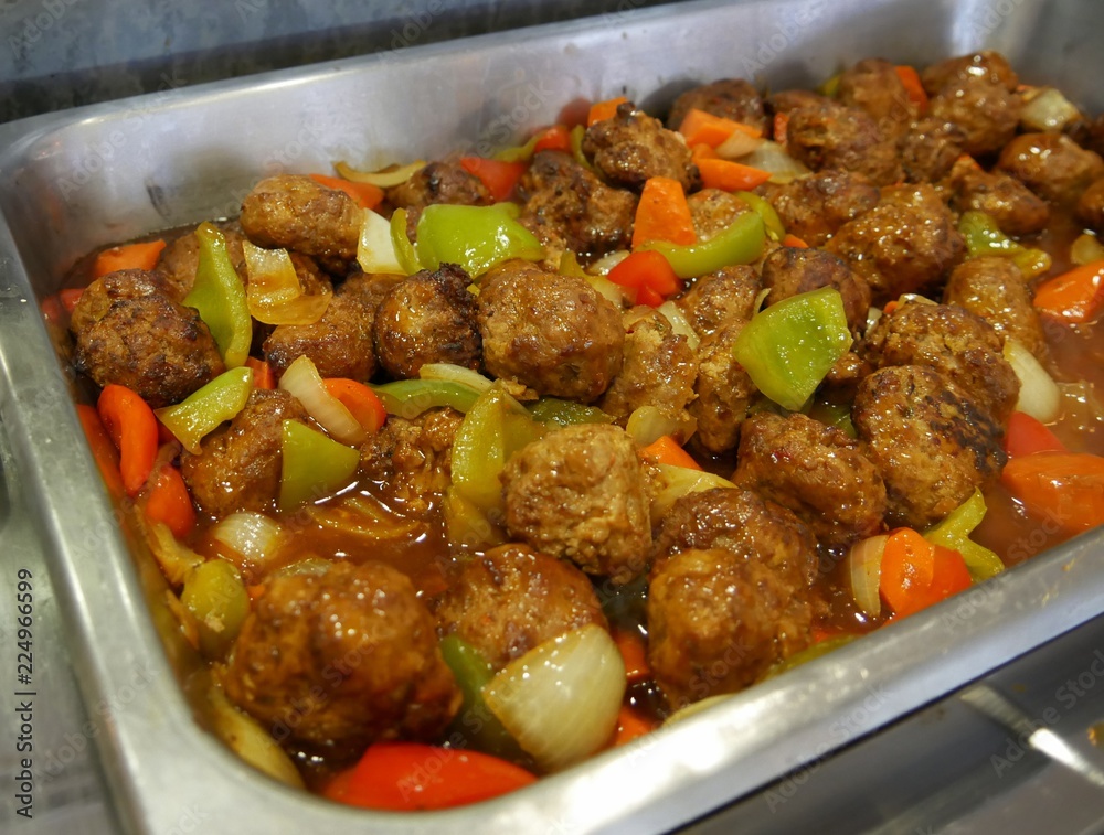 Meatballs in sauce with sliced onions, green and red peppers in a rectangular metal tray