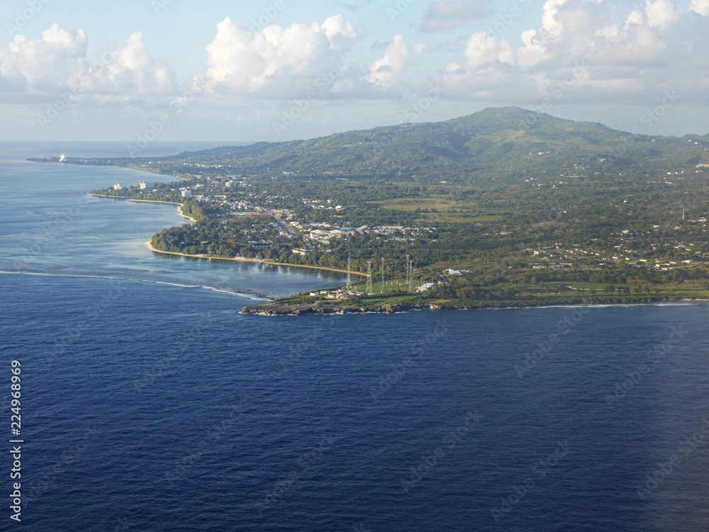 Aerial view of Saipan western coast from a distance, with the deep blue waters of the Saipan-Tinian channel in between