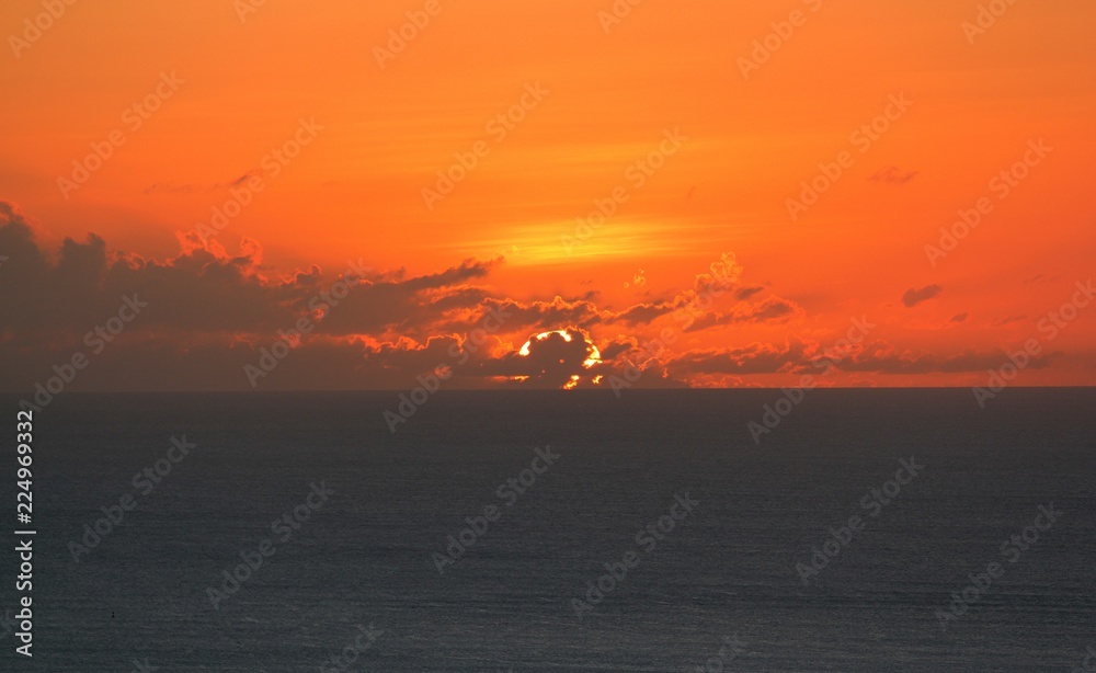 A big full sun sets behind orange and golden clouds in a tropical island