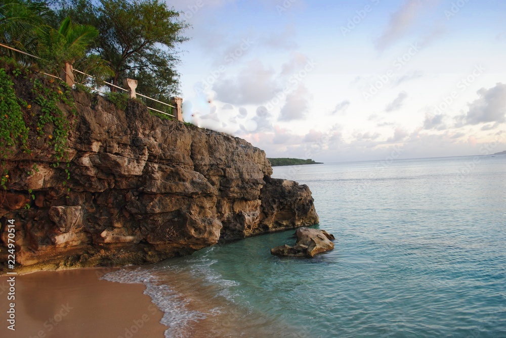 Rocky cliff walls of Taga Beach with the beautiful cove below, boasting of clear waters and soft white sand