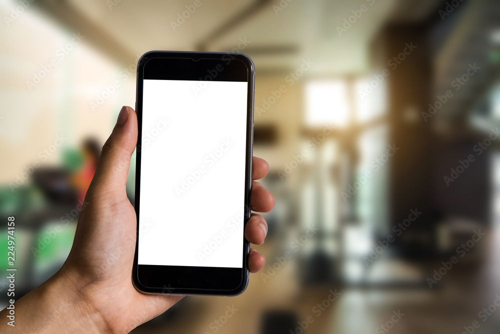 Hand holding white mobile phone with blank white screen at the corner of the gym. Hand holding white mobile phone with blank white screen at the corner of the gym.