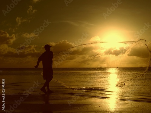 Silhouette of an unrecognizable man throwing out his fishing net from the shore of the Saipan lagoon at sunset, Northern Mariana Islands.
