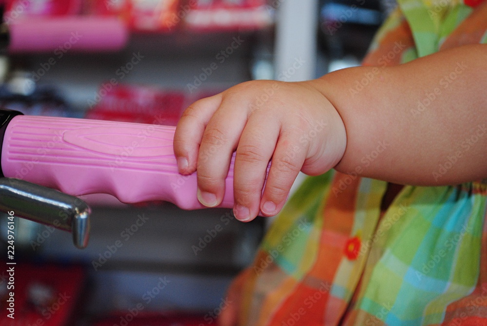 A baby girl’s chubby hand holding the pink handlebar of a bicycle