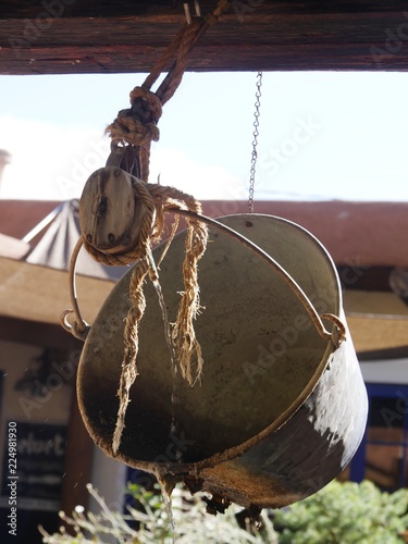 Old metal bucket hanging from ropes above a wishing well in a park photo