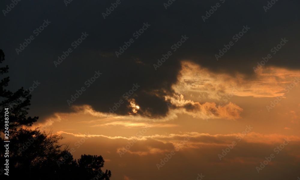 Fototapeta premium The setting sun partially hidden by dark clouds in the skies