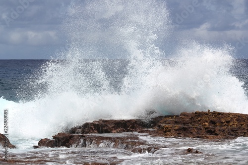 Close up of a giant splash of waves breaking against a coral platform at the beach of a tropical island 