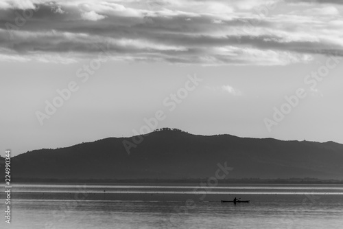 Beautiful view of Trasimeno lake at sunset with birds on water, a man on a canoe and hills on the background