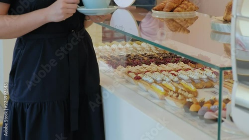 She buyer chooses yummy. Young attractive girl, woman buys in the coffee shop or pastries, cakes, cake, macaroon. A buyer standing under a a glass case at the bakery, coffee shop