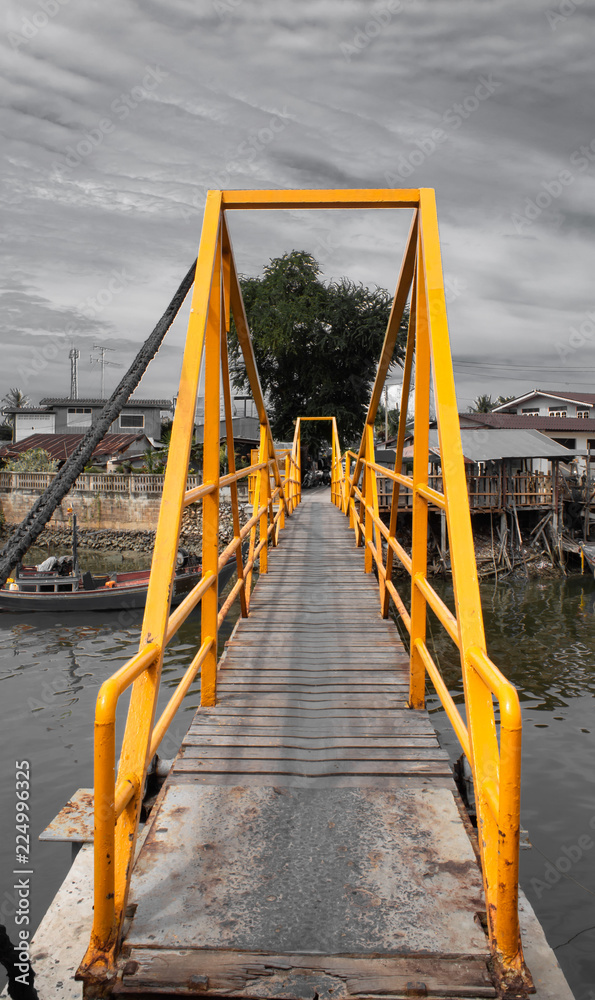 A wooden bridge over the canal The steel building painted yellow cattle. A wooden bridge over the canal The steel building painted yellow cattle.