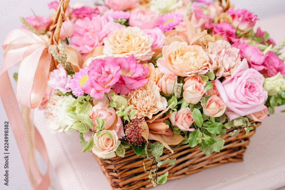 flowers arrangement with various of colors in wicker basket on pink table. beautiful spring bouquet. bright room, white wall. copy space flowers arrangement with various of colors in wicker basket on pink table. beautiful spring bouquet. bright room, white wall. copy space