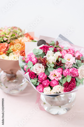 two beautiful spring bouquet. flowers arrangements with various of colors in glass vase on pink table. bright room, white wall
