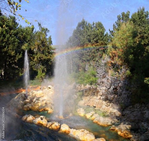 Jets of water spew out of a fountain in a river at a park,with a rainbow 