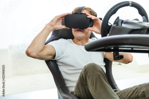 A young, handsome guy in a white T-shirt, playing in a race, on a simulator of virtual reality
