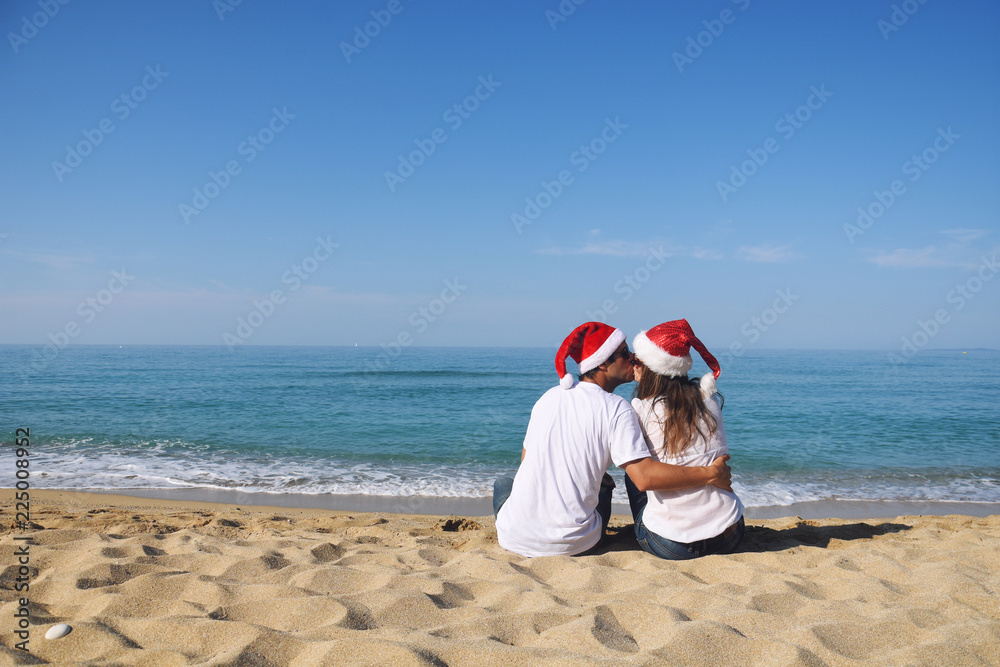 Happy Couple with Santa hat at beach. Young couple in love celebrate Christmas on beach Happy Couple with Santa hat at beach. Young couple in love celebrate Christmas on beach