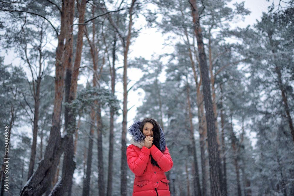 Beautiful girl in a pink jacket standing in a forest among tall Christmas trees