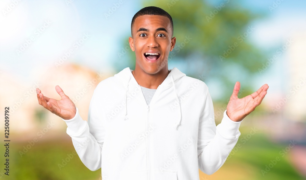 Dark-skinned young man with white sweatshirt with surprise and shocked facial expression. Mouth open because not expect what has happened in a park Dark-skinned young man with white sweatshirt with surprise and shocked facial expression. Mouth open because not expect what has happened in a park