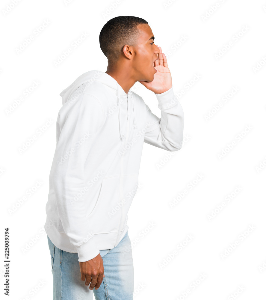 Dark-skinned young man with white sweatshirt shouting with mouth wide open to the lateral and announcing something on isolated white background Dark-skinned young man with white sweatshirt shouting with mouth wide open to the lateral and announcing something on isolated white background