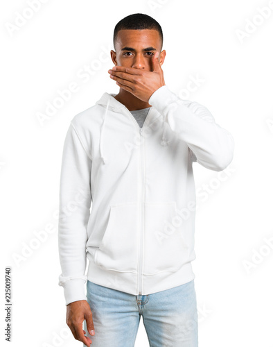 Dark-skinned young man with white sweatshirt covering mouth with hands for saying something inappropriate. Can not speak on isolated white background