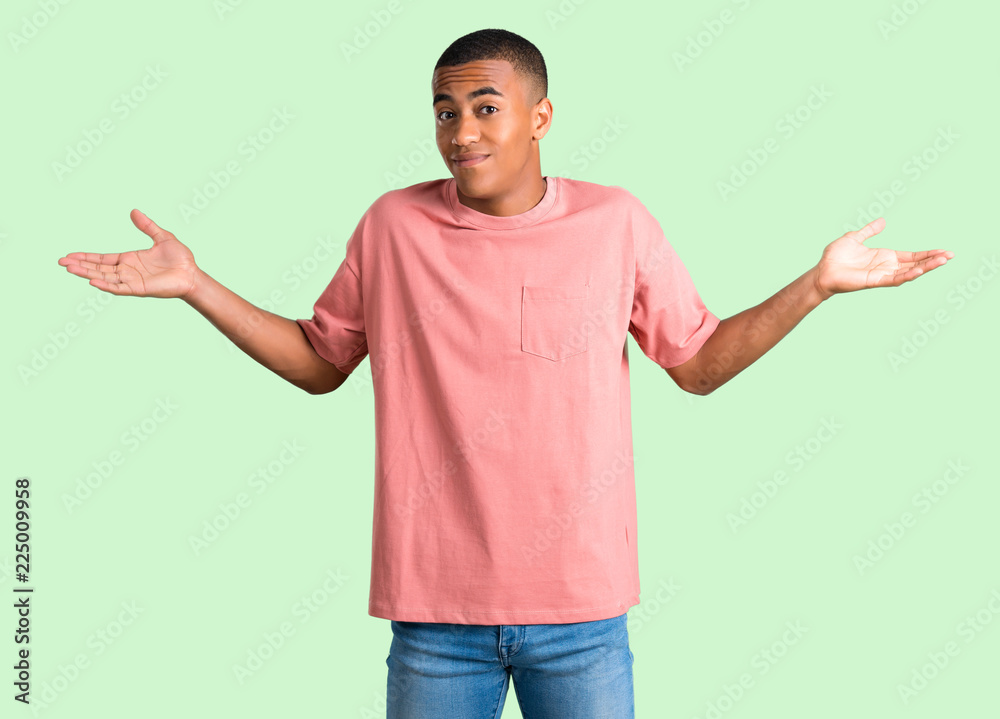 Dark skinned man making unimportant and doubts gesture while lifting the shoulders and the palms of the hands on green isolated background Dark skinned man making unimportant and doubts gesture while lifting the shoulders and the palms of the hands on green isolated background