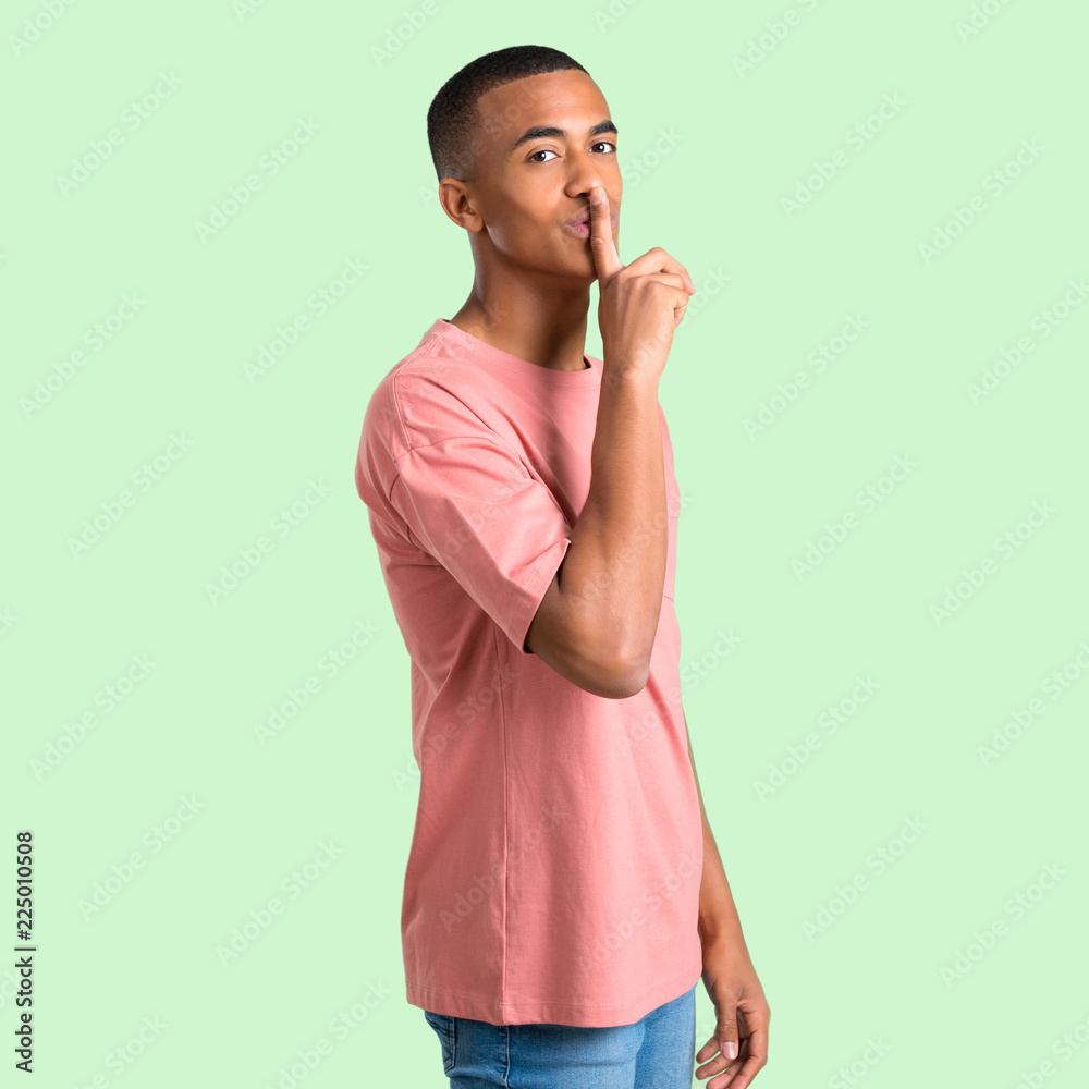 Dark skinned man showing a sign of closing mouth and silence gesture putting finger in mouth on green isolated background Dark skinned man showing a sign of closing mouth and silence gesture putting finger in mouth on green isolated background