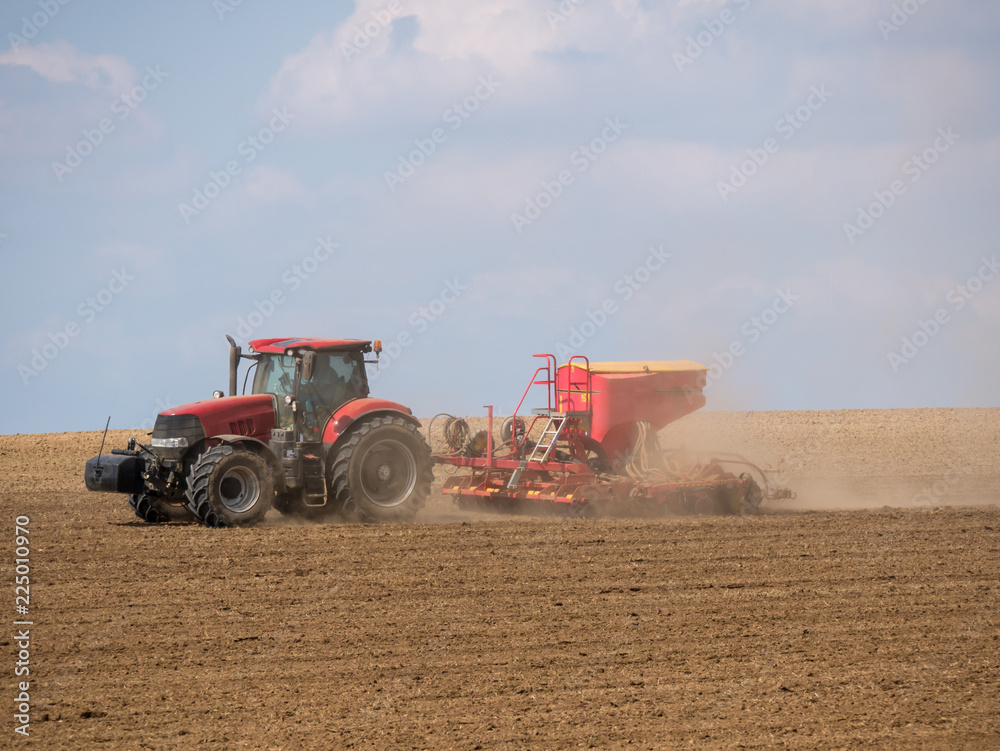 Tractor with a modern sowing seeds machine in a newly plowed field. Plowed land as a background. Red tractor on the field. Tractor with a modern sowing seeds machine in a newly plowed field. Plowed land as a background. Red tractor on the field.