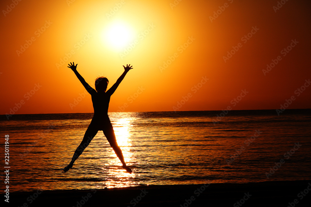 Silhouette of a jumping woman against the background of the setting sun over the sea.