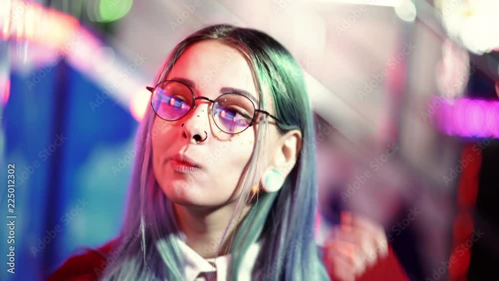Hipster girl with blue dyed hair and golden sequins as freckles puts on transparent glasses and builds pretty face. Woman with nose piercing,, ears tunnels, unusual hairstyle Hipster girl with blue dyed hair and golden sequins as freckles puts on transparent glasses and builds pretty face. Woman with nose piercing,, ears tunnels, unusual hairstyle