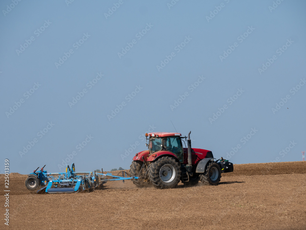 Obraz premium Red tractor with plow on the field. Tractor on the field. Summer field and red tractor.