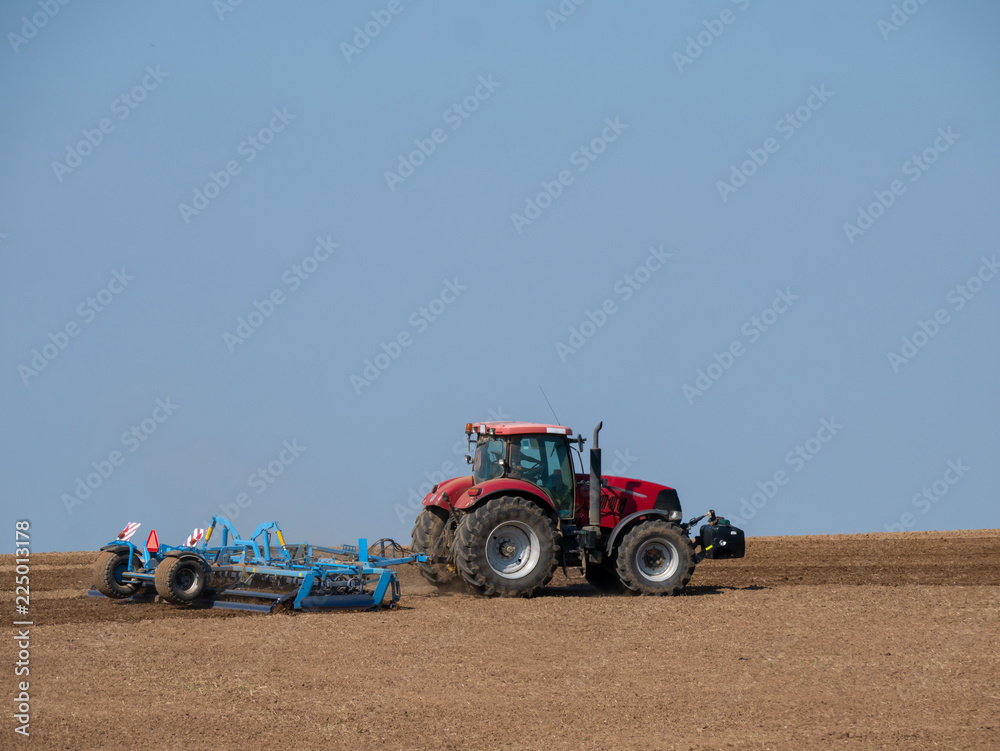 Obraz premium Red tractor with plow on the field. Tractor on the field. Summer field and red tractor.