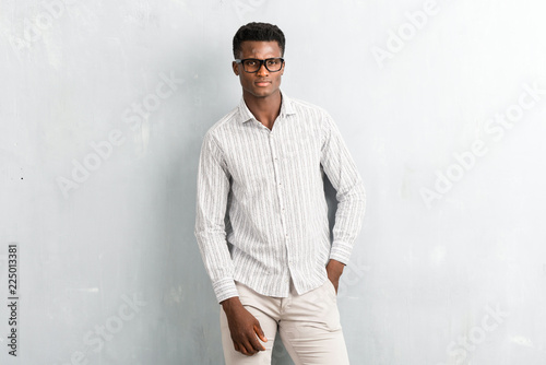 Young afro american man with glasses posing on textured grey wall