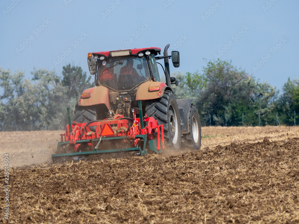 Fototapeta premium Red tractor with plow on the field. Tractor on the field. Summer field and red tractor.