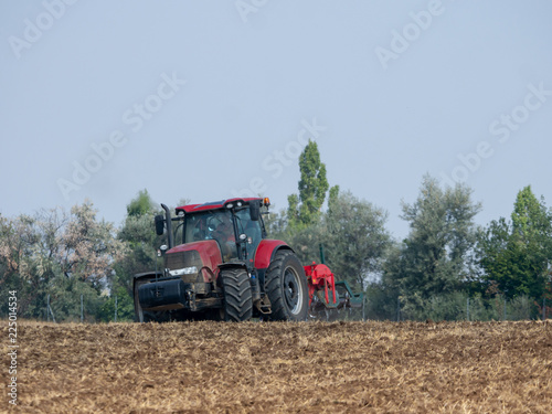 Red tractor with plow on the field. Tractor on the field. Summer field and red tractor.