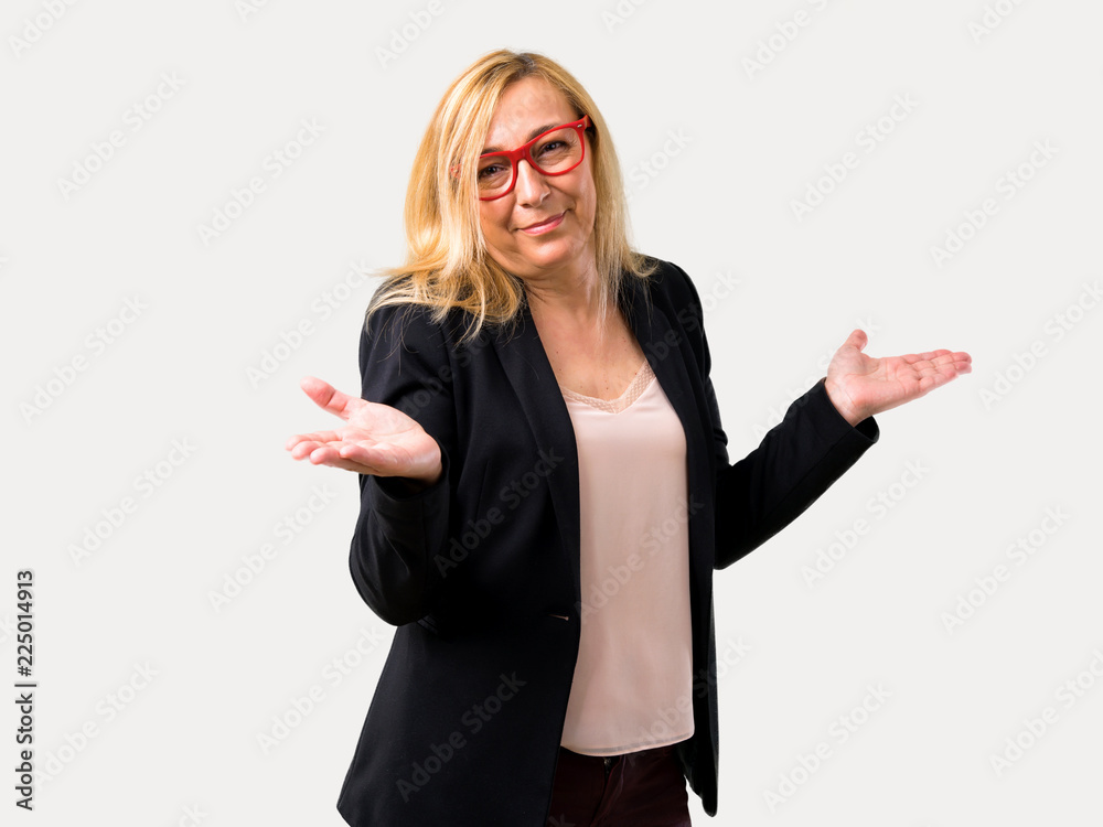 Middle-age blonde business woman with black jacket making unimportant and doubts gesture while lifting the shoulders and the palms of the hands on isolated grey background Middle-age blonde business woman with black jacket making unimportant and doubts gesture while lifting the shoulders and the palms of the hands on isolated grey background