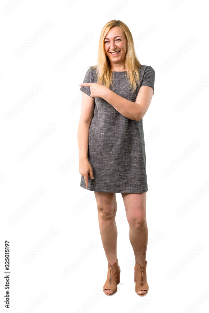 Middle age blonde woman with grey dress pointing finger to the side and presenting a product on isolated white background Middle age blonde woman with grey dress pointing finger to the side and presenting a product on isolated white background