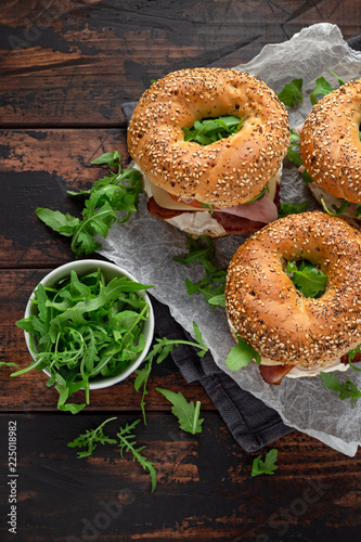 Fresh Bagels Sandwiches with cream cheese, bacon, tomato and green wild rocket on rustic wooden table