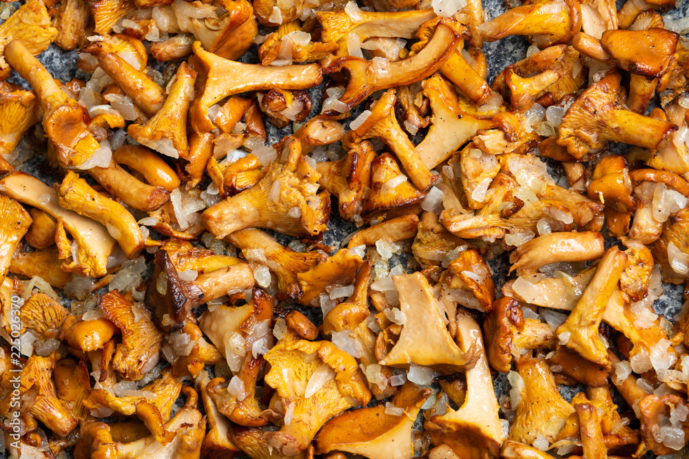 Fototapeta premium Top view of fried chanterelle mushrooms with onion bites on a frying pan.