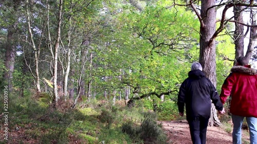 middle aged couple walking through a woodland with autumn colours on trees.