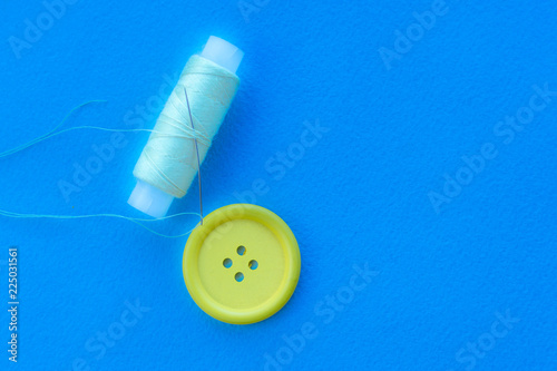Yellow button and spool of thread on a blue background.