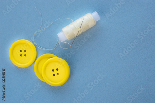 Three yellow buttons and a spool of thread on a blue background.