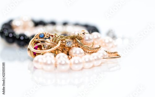 Real gold jewlery, diamonds, gems, rings, neckless with pearls close up shot , white background, on shiny surface.