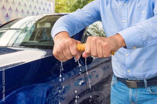 A man unscrews a rag, on a background a car. A man cleaning car with microfiber cloth. Man holds the microfiber in hand