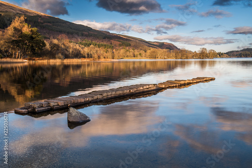 The old stone jetty on the shore of a very still Loch Ard. Stirlingshire  Scotland