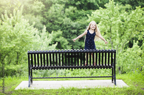 Bild auf Leinwand Portrait of smiling little girl standing on black bench outdoors