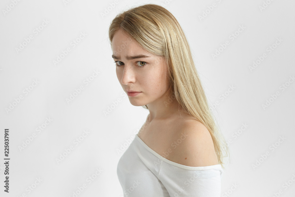 Profile studio shot of beautiful woman with blonde loose hair posing isolated having worried tense facial expression, experiencing some problem, suffering from headache, looking at camera and frowning