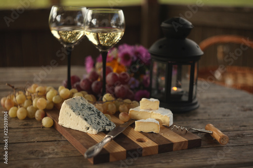 wine in a bottle a glasses of white wine  grapes various cheese and  blue cheese cheese Camembert  a bouquet and a lantern on the old table