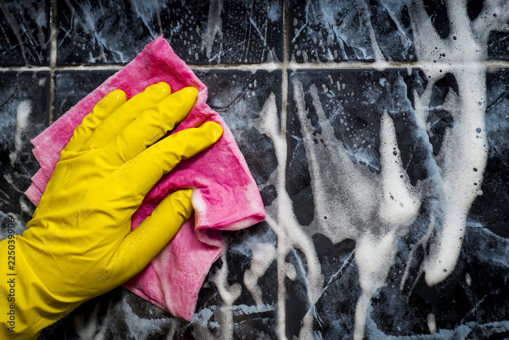 A human hand in a yellow rubber glove washes a tiled cloth Stock Photo
