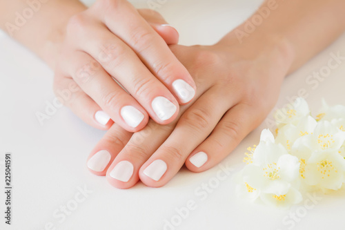 Young  perfect woman s hands with white nails. Care about nails and clean  soft  smooth skin. Manicure  pedicure beauty salon. Beautiful jasmine blossoms on table. Fresh flowers.